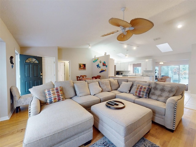 living room with ceiling fan, vaulted ceiling with skylight, and light wood-type flooring