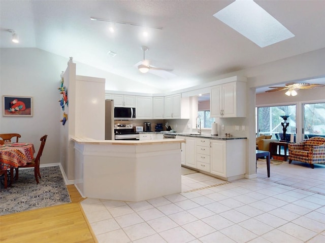 kitchen with white cabinetry, lofted ceiling with skylight, ceiling fan, and appliances with stainless steel finishes