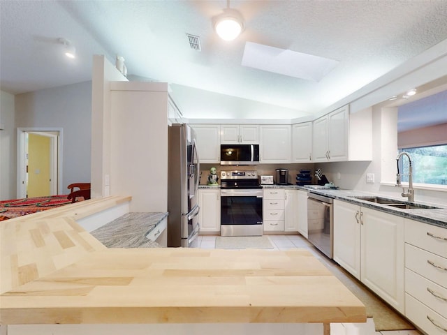 kitchen featuring sink, appliances with stainless steel finishes, lofted ceiling with skylight, white cabinets, and kitchen peninsula