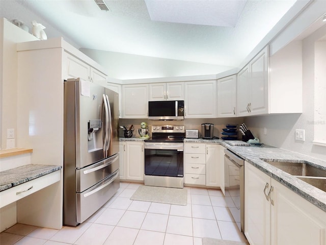 kitchen with light tile patterned flooring, vaulted ceiling, appliances with stainless steel finishes, light stone countertops, and white cabinets