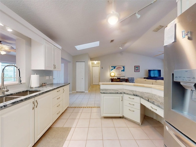 kitchen with stainless steel refrigerator with ice dispenser, light tile patterned floors, sink, and white cabinets