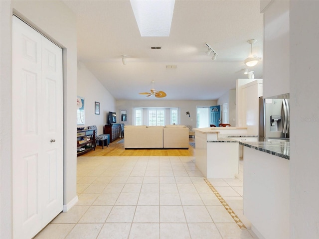 kitchen featuring lofted ceiling with skylight, white cabinets, light tile patterned flooring, stainless steel fridge with ice dispenser, and kitchen peninsula