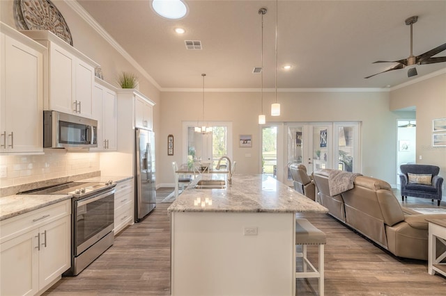 kitchen featuring stainless steel appliances, white cabinetry, a kitchen island with sink, and pendant lighting