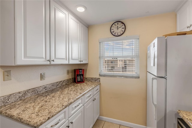 kitchen with light tile patterned floors, light stone countertops, white cabinets, and white refrigerator