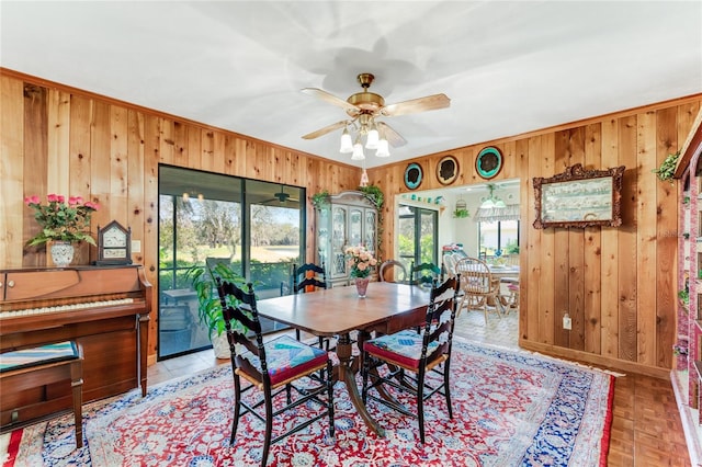 dining area featuring ceiling fan, a wealth of natural light, and wood walls