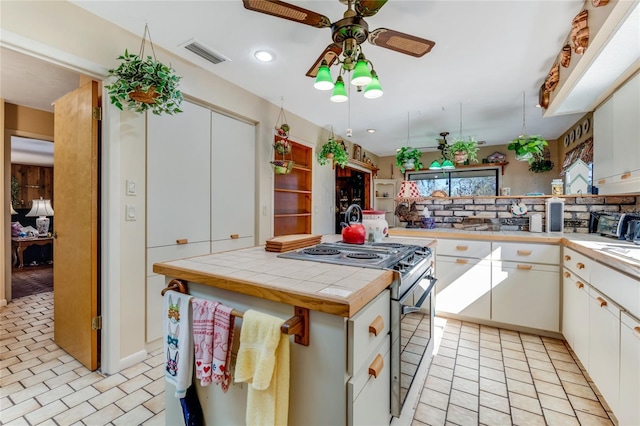 kitchen featuring stainless steel electric range oven, a kitchen island, tile countertops, tasteful backsplash, and white cabinetry