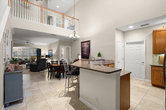 kitchen with light tile patterned flooring, a breakfast bar, ceiling fan with notable chandelier, pendant lighting, and sink