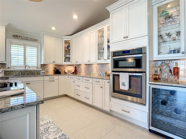 kitchen featuring wine cooler, sink, light stone counters, stainless steel double oven, and white cabinets