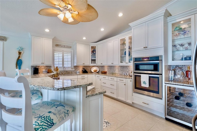 kitchen featuring sink, white cabinetry, backsplash, light stone countertops, and a kitchen bar