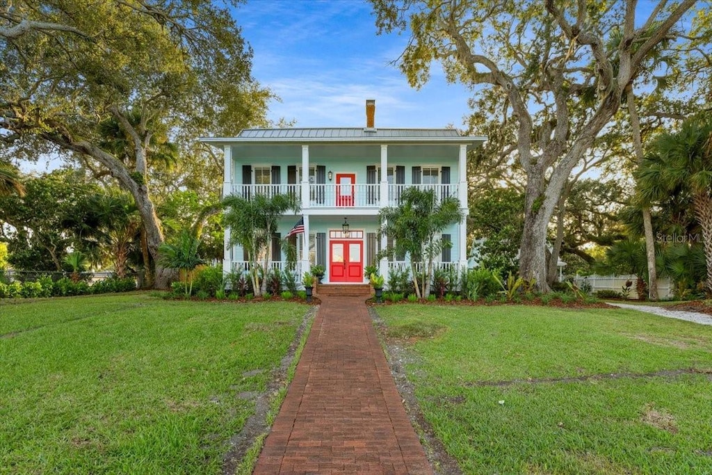 view of front of house featuring french doors, a balcony, and a front lawn