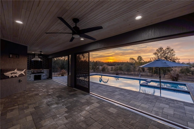 patio terrace at dusk featuring ceiling fan, exterior kitchen, and a pool with hot tub