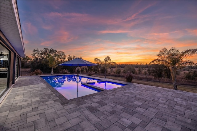 pool at dusk with a patio and an in ground hot tub