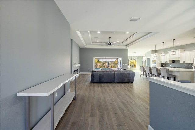 living room featuring sink, wood-type flooring, a raised ceiling, and ceiling fan