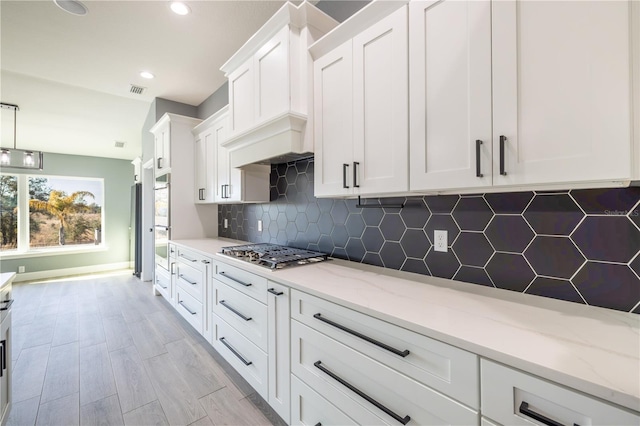 kitchen with light stone counters, decorative backsplash, stainless steel gas cooktop, and white cabinets