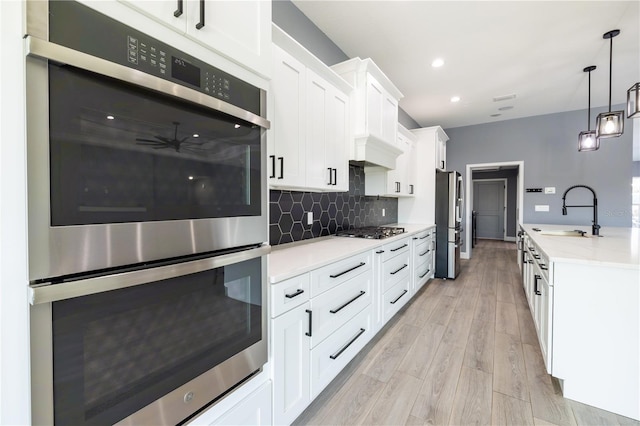 kitchen with sink, appliances with stainless steel finishes, white cabinetry, backsplash, and decorative light fixtures