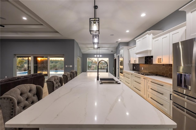 kitchen featuring sink, light stone counters, a large island with sink, appliances with stainless steel finishes, and pendant lighting