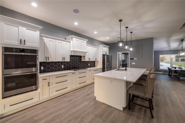 kitchen with pendant lighting, a breakfast bar, stainless steel appliances, white cabinets, and a center island with sink