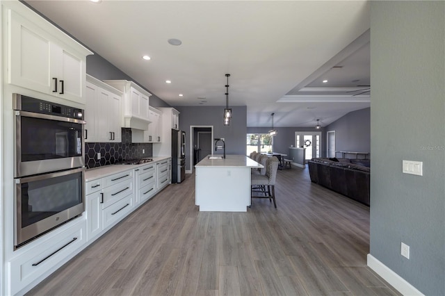 kitchen featuring sink, white cabinetry, decorative light fixtures, an island with sink, and stainless steel appliances