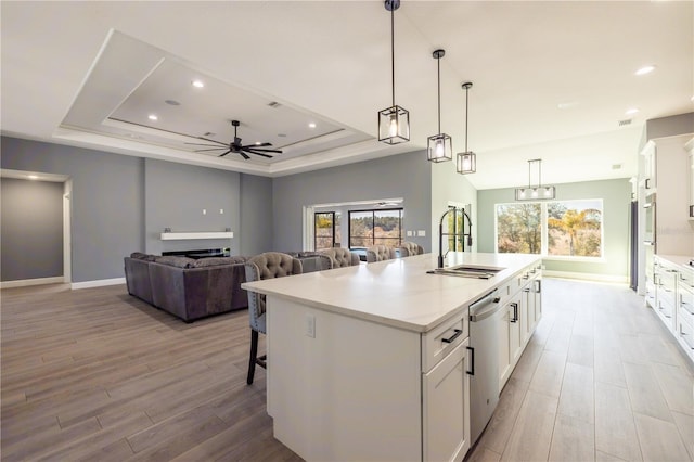 kitchen featuring sink, white cabinetry, hanging light fixtures, a tray ceiling, and a kitchen island with sink