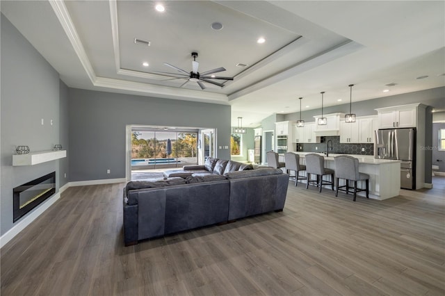 living room with sink, dark wood-type flooring, a raised ceiling, and ceiling fan