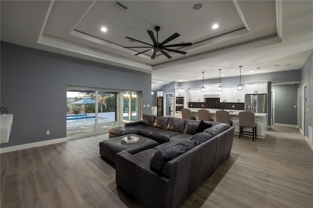 living room featuring crown molding, ceiling fan, a tray ceiling, and light hardwood / wood-style floors