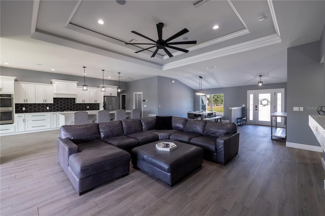 living room with crown molding, a raised ceiling, ceiling fan with notable chandelier, and light hardwood / wood-style flooring