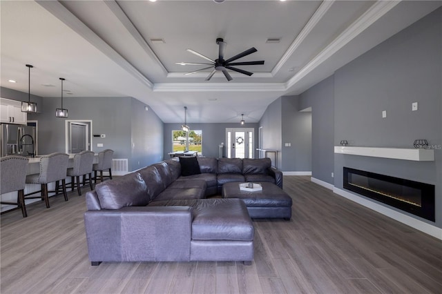 living room with ceiling fan, ornamental molding, light hardwood / wood-style floors, and a tray ceiling