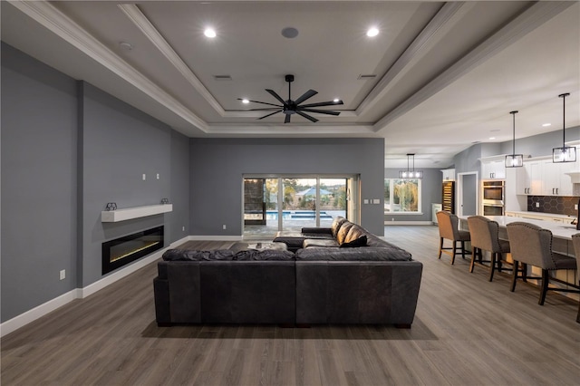 living room with a raised ceiling, ornamental molding, hardwood / wood-style floors, and ceiling fan