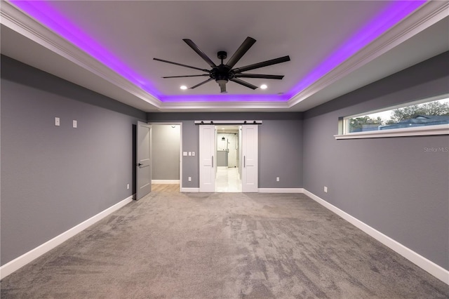 interior space featuring carpet flooring, ornamental molding, ceiling fan, a tray ceiling, and a barn door