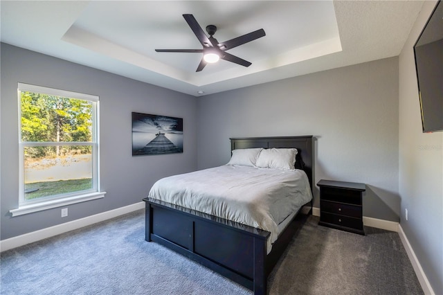 bedroom featuring dark carpet, a tray ceiling, and ceiling fan