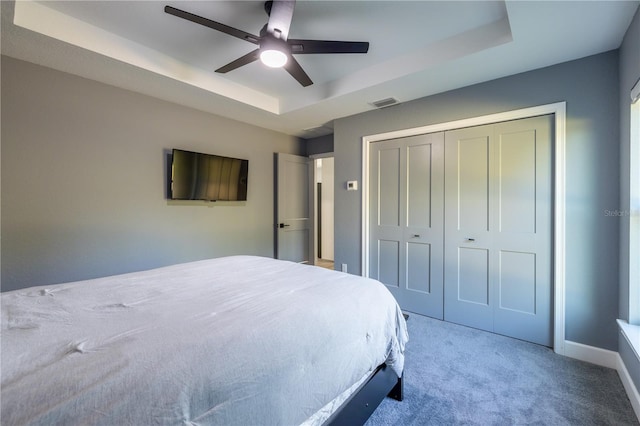 carpeted bedroom featuring ceiling fan, a tray ceiling, and a closet