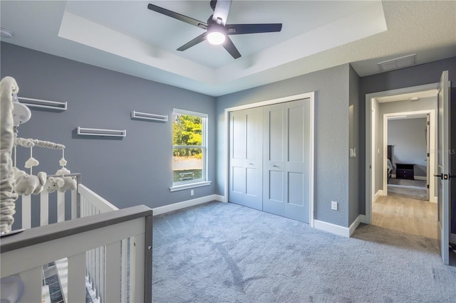 bedroom featuring a closet, carpet, ceiling fan, and a tray ceiling