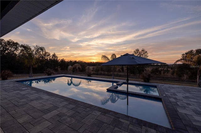 pool at dusk featuring an in ground hot tub and a patio