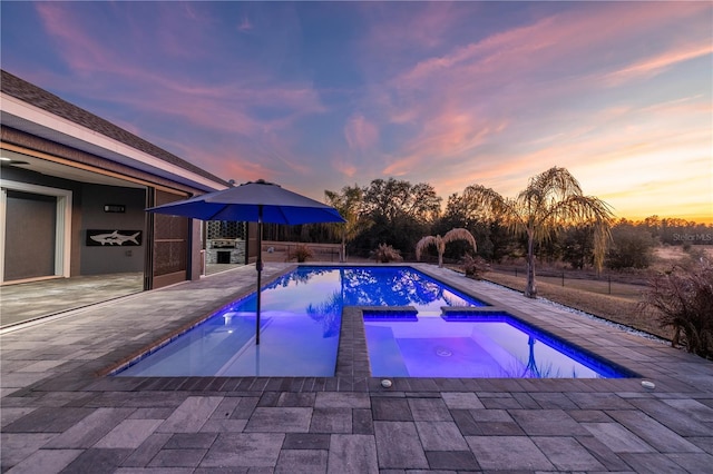 pool at dusk featuring an in ground hot tub and a patio