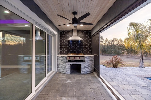 patio terrace at dusk featuring area for grilling, ceiling fan, and exterior kitchen