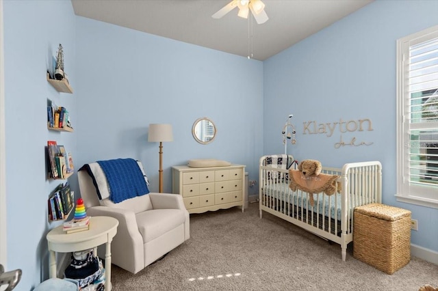 bedroom featuring a nursery area, light colored carpet, and ceiling fan