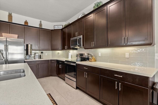 kitchen with light tile patterned floors, decorative backsplash, dark brown cabinets, and appliances with stainless steel finishes