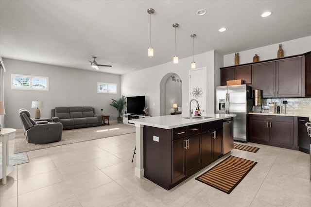 kitchen with decorative light fixtures, an island with sink, sink, stainless steel fridge, and dark brown cabinets