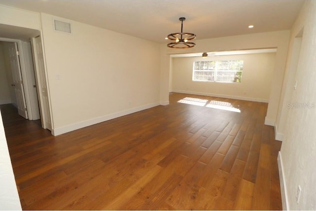 empty room with dark wood-type flooring and a chandelier