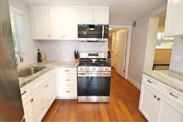 kitchen featuring sink, hardwood / wood-style flooring, appliances with stainless steel finishes, white cabinetry, and light stone countertops