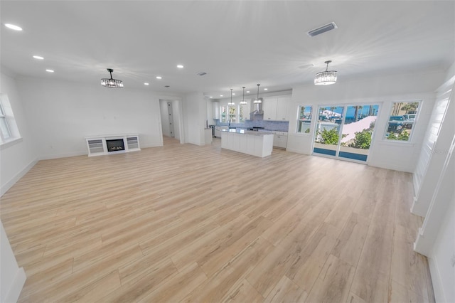 unfurnished living room with recessed lighting, a fireplace, visible vents, light wood-style floors, and an inviting chandelier