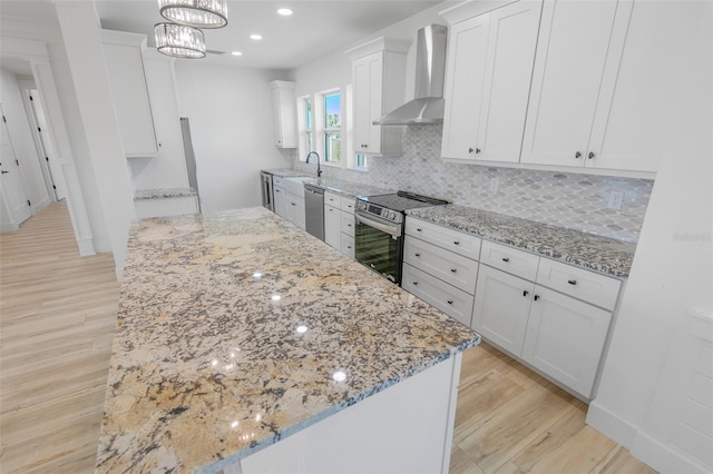 kitchen with appliances with stainless steel finishes, wall chimney range hood, white cabinetry, and pendant lighting