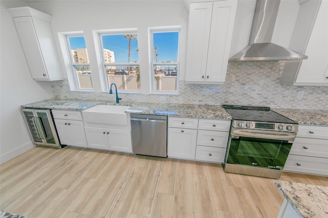 kitchen with white cabinets, wall chimney exhaust hood, stainless steel appliances, light wood-style floors, and a sink