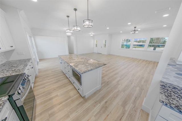 kitchen with stainless steel appliances, white cabinets, open floor plan, a center island, and pendant lighting