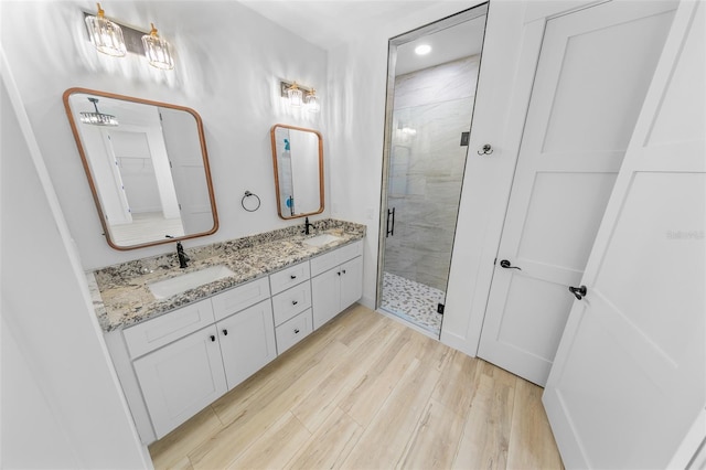 bathroom with double vanity, a sink, a shower stall, and wood finished floors