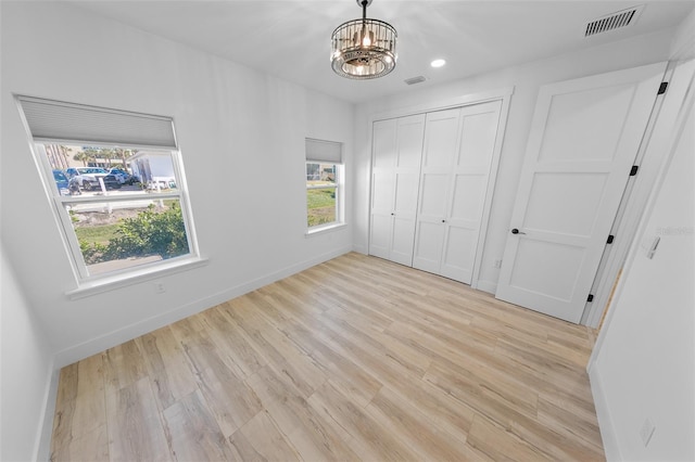 unfurnished bedroom with baseboards, visible vents, a notable chandelier, light wood-type flooring, and a closet