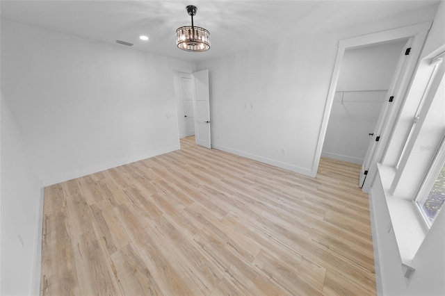 unfurnished bedroom featuring a notable chandelier, visible vents, baseboards, a spacious closet, and light wood finished floors