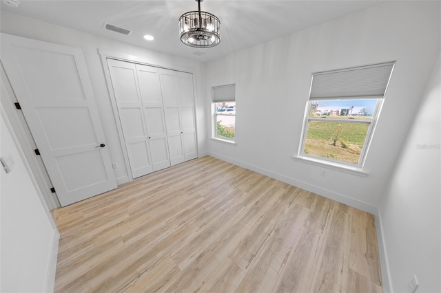 unfurnished bedroom featuring light wood finished floors, baseboards, visible vents, a notable chandelier, and a closet