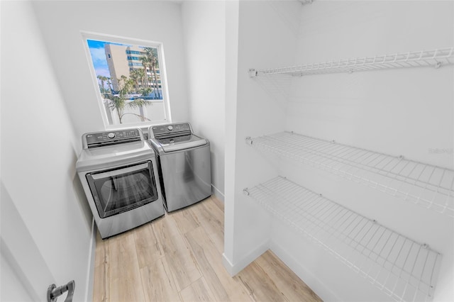 clothes washing area with light wood-type flooring, washing machine and dryer, laundry area, and baseboards