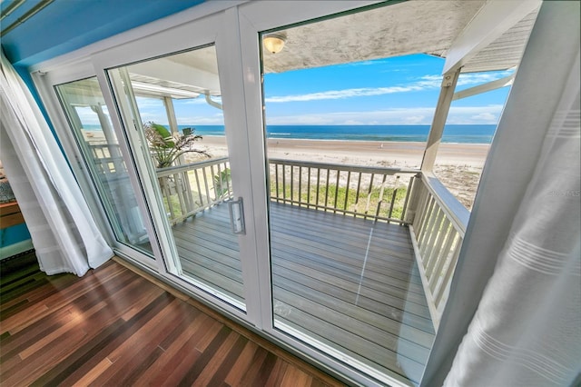 doorway with a water view, dark wood-type flooring, and a view of the beach